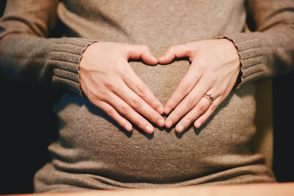 Kvinna håller händerna i ett hjärta över sin gravida mage. 